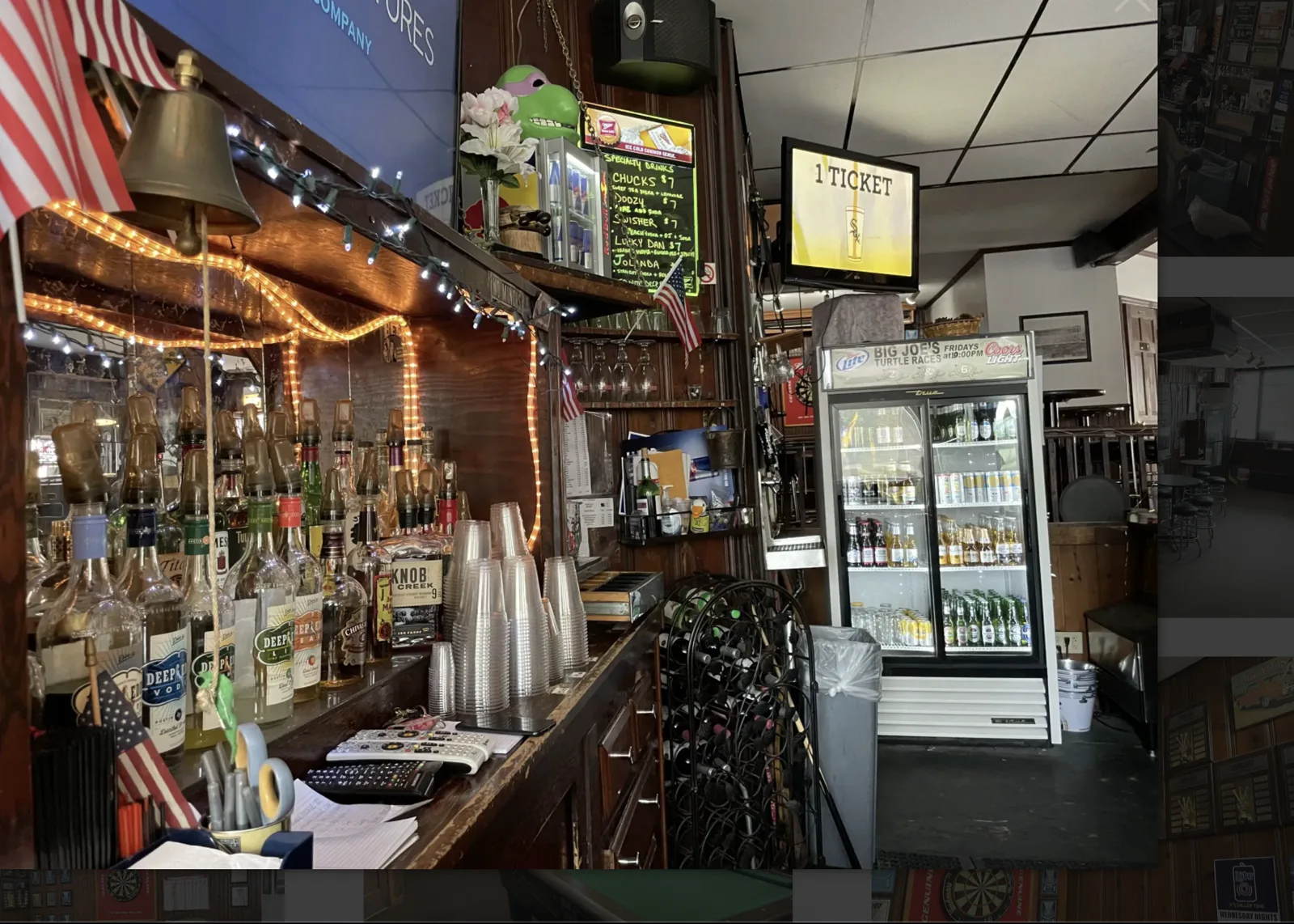 The rail at Big Joe's, with a Friday turtle-race fridge sign, liquor bottles, and wood-paneled dart wall