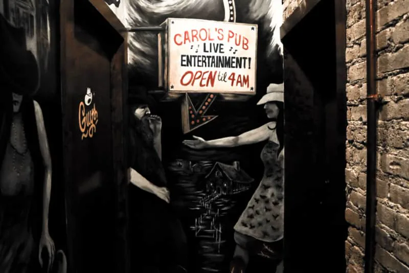 A lighted Carol's Pub live-entertainment sign and country murals in the hallway