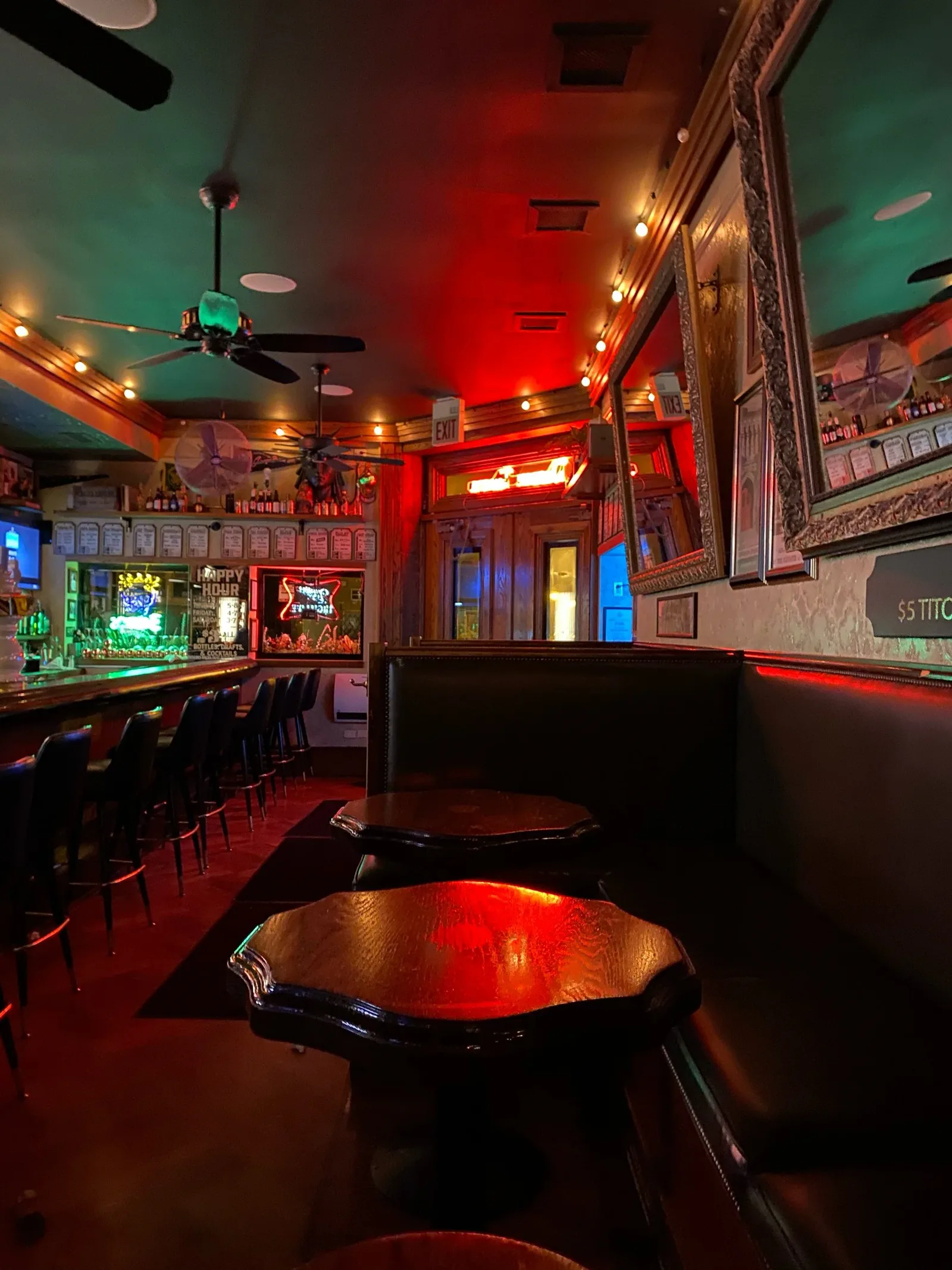 Empty cloverleaf tables, a vinyl booth, and red-green tavern light inside Damen Tavern