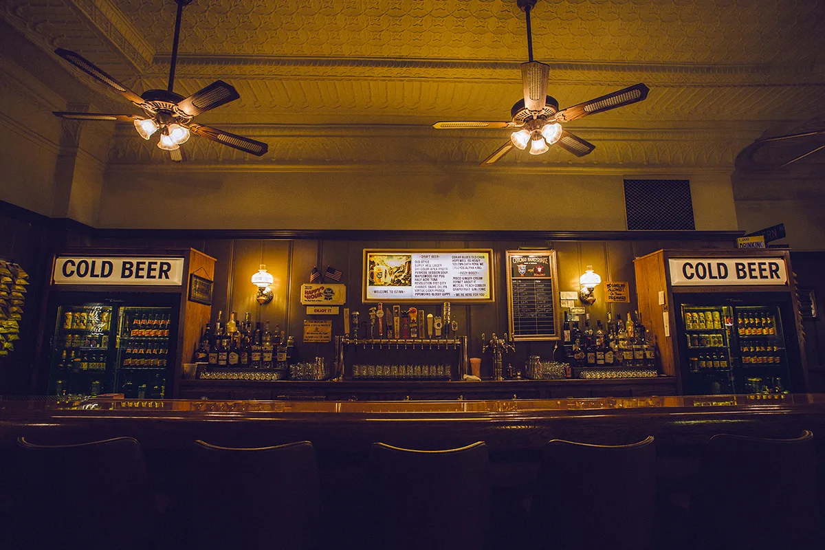 Empty stools and the Welcome to EZ Inn draft board between two COLD BEER coolers