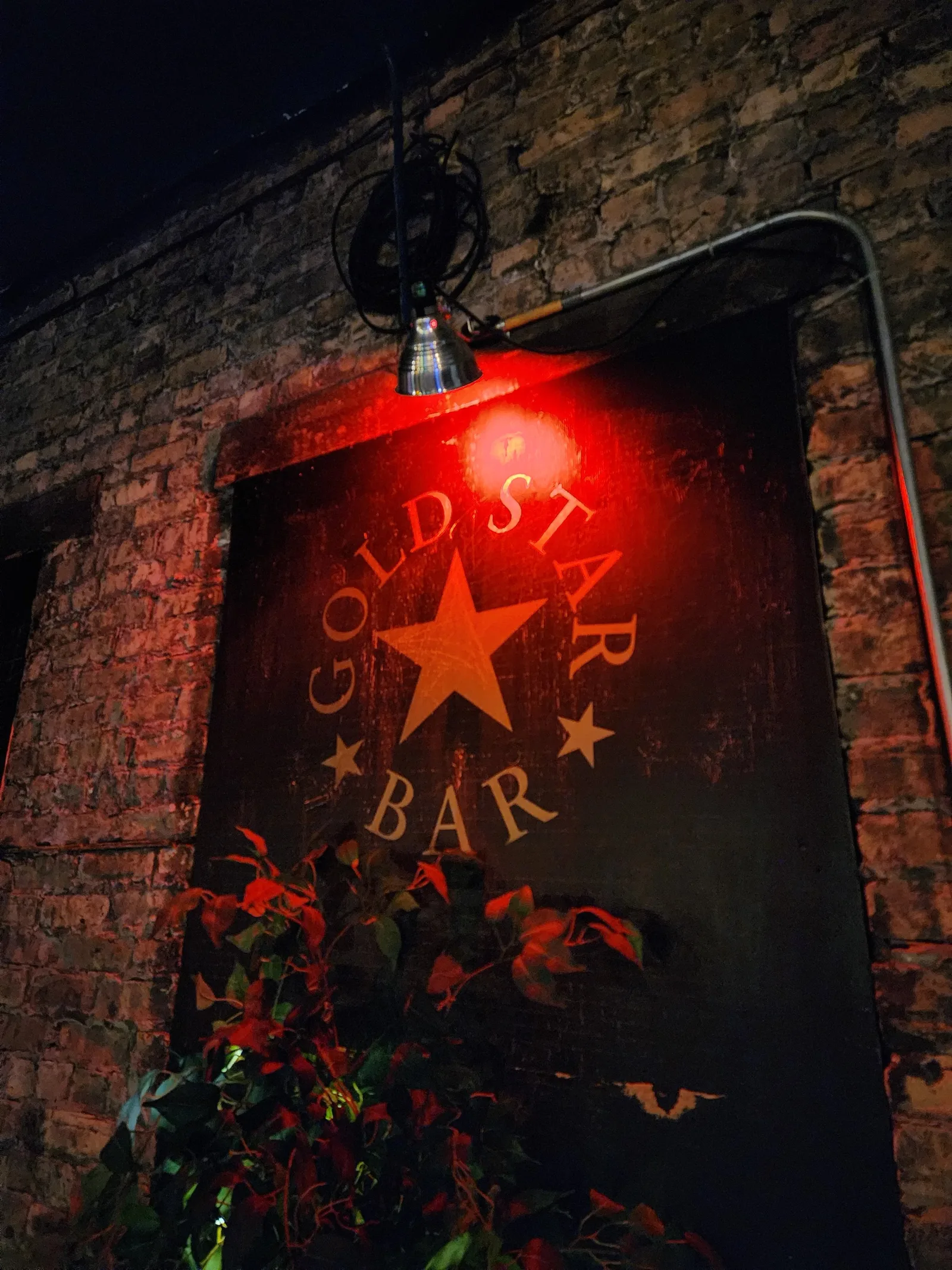The Gold Star Bar wall sign on brick, lit from above