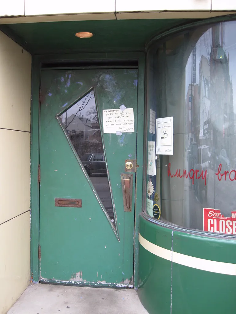 The Hungry Brain door with its triangular window and a handwritten note not to lock bikes next door