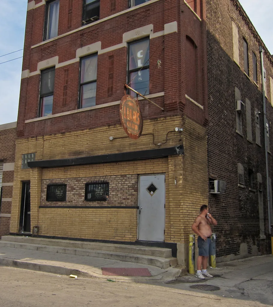 The tan-brick storefront, barred windows, and hanging Liar's Club sign on Fullerton Avenue