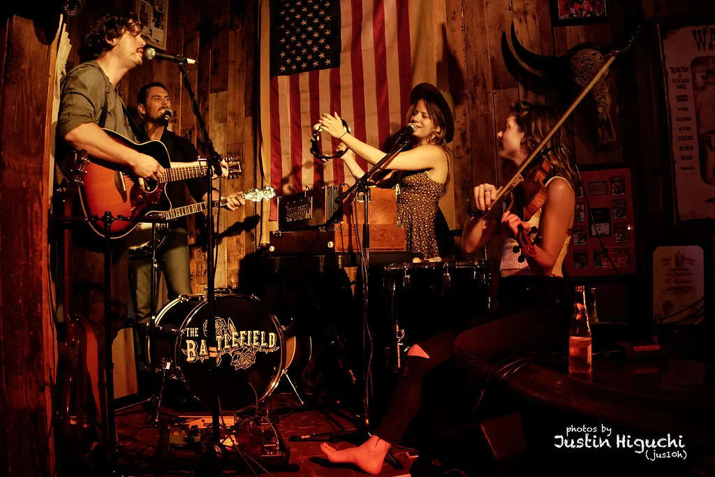 The Battlefield on stage at The Escondite on August 13, 2016, under string lights with a red exit sign