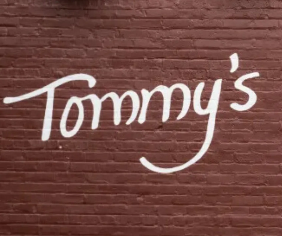 The hand-painted white Tommy's script on the maroon brick wall