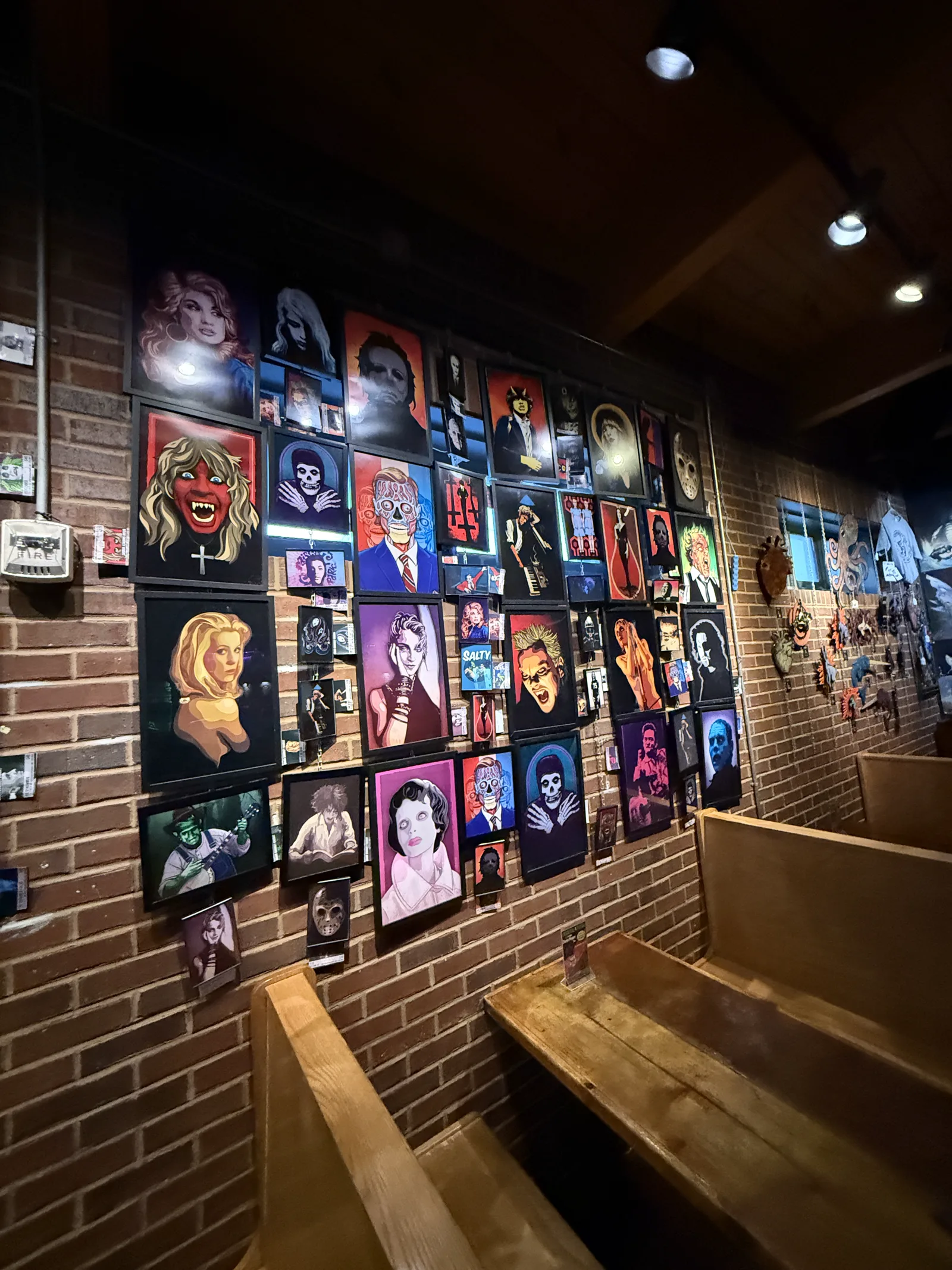 A brick wall covered in framed pop-culture and horror portraits at Trackside Tavern